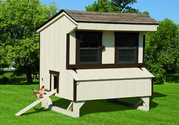 A rooster is walking into a tan chicken coop with brown detailing.